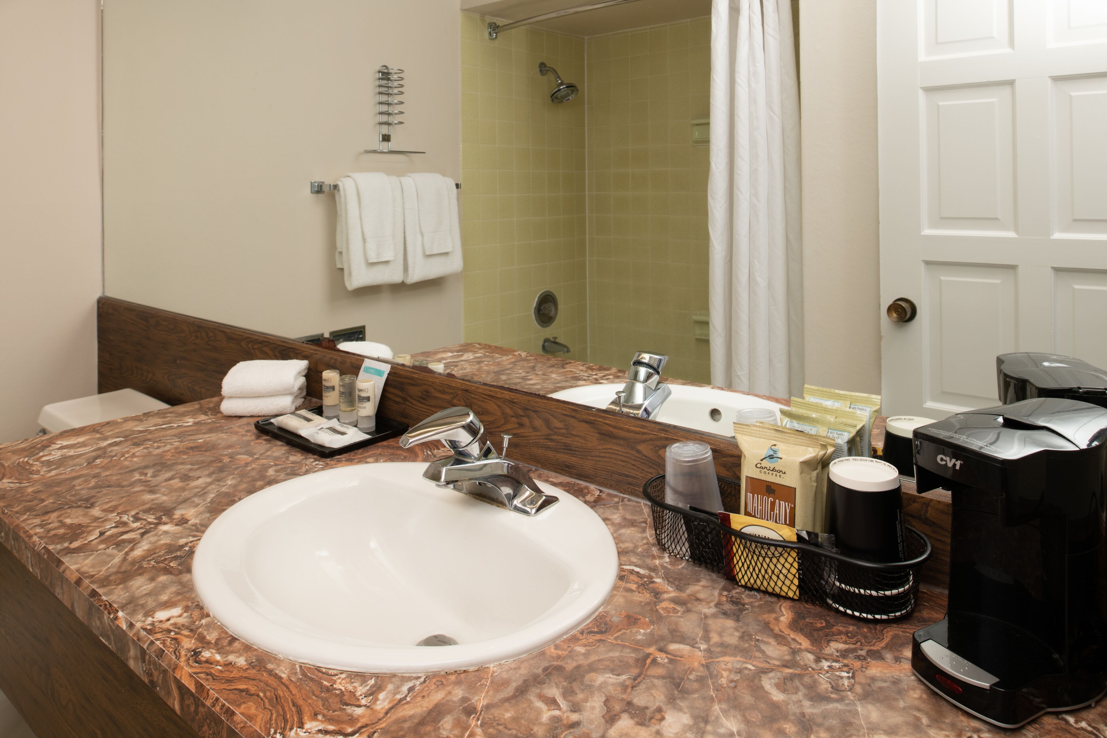 A bathroom with a marble sink, a mirror, a shower, and toiletries.