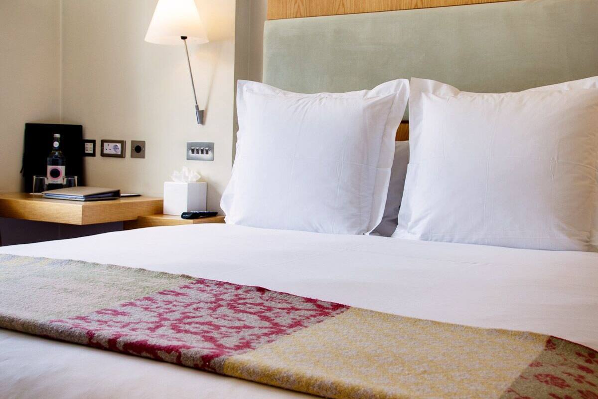 A hotel room with a neatly made bed, a bedside table with a lamp, and a wall-mounted power outlet.