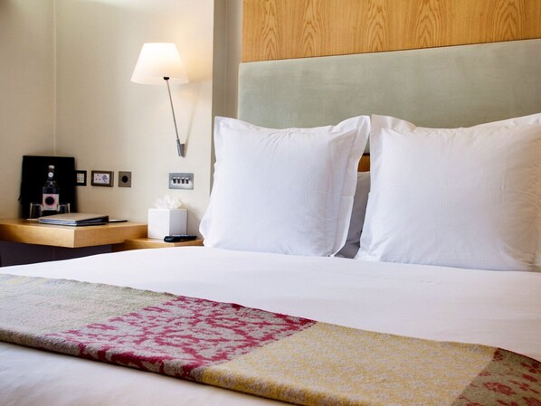 A hotel room with a neatly made bed, a bedside table with a lamp, and a wall-mounted power outlet. - Sydney House Chelsea (London)