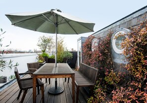 An outdoor patio with a wooden table, chairs, and a large umbrella. - Sydney House Chelsea (London)