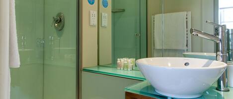 A modern bathroom with a glass shower enclosure, a white sink with a mirror above, and a glass-topped vanity.