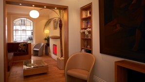 A cozy living room with a sofa, a coffee table, a bookshelf, and a large painting. - Sydney House Chelsea (London)