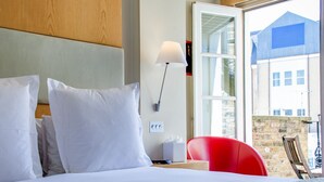 A hotel room with a large bed, a red chair, a lamp, and a view of buildings outside the window. - Sydney House Chelsea (London)