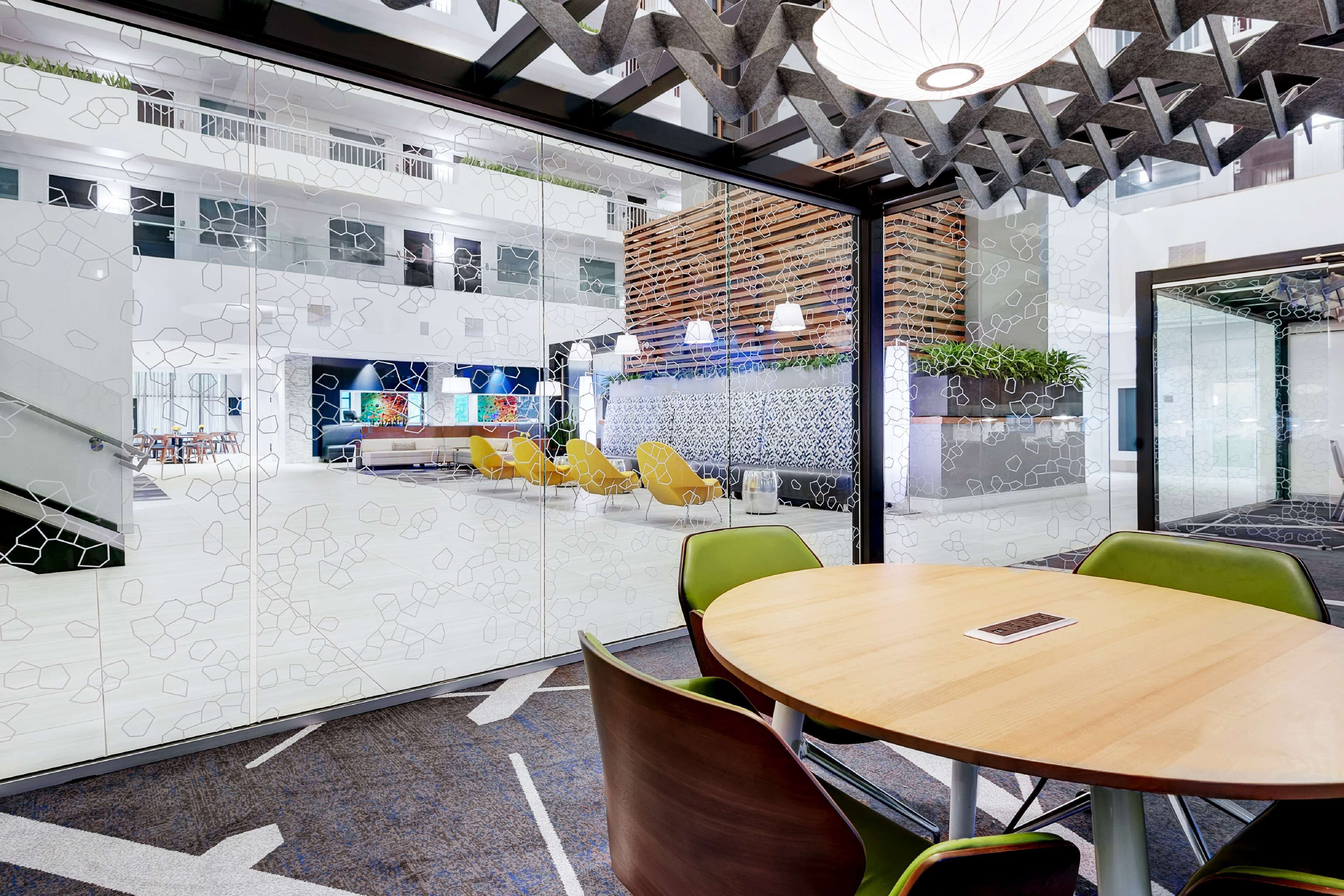 A modern office space with a glass partition, green and yellow chairs, and a wooden table.