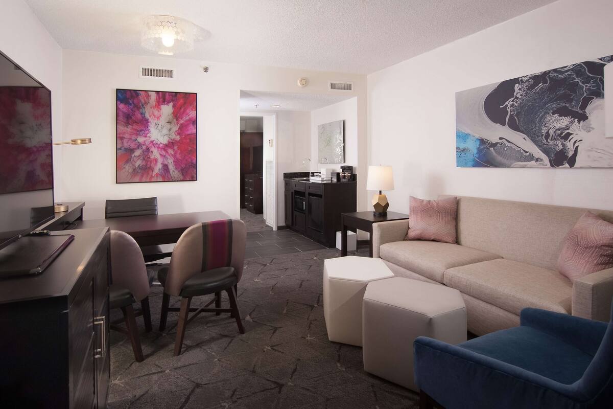 A modern hotel room with a dining area, a sofa, a coffee table, and artwork on the walls.