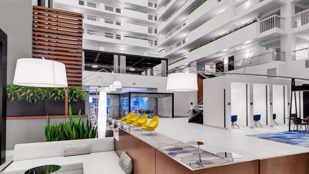 Un hall d’hôtel moderne avec un comptoir d’accueil central, un espace salon et un escalier menant aux étages supérieurs.