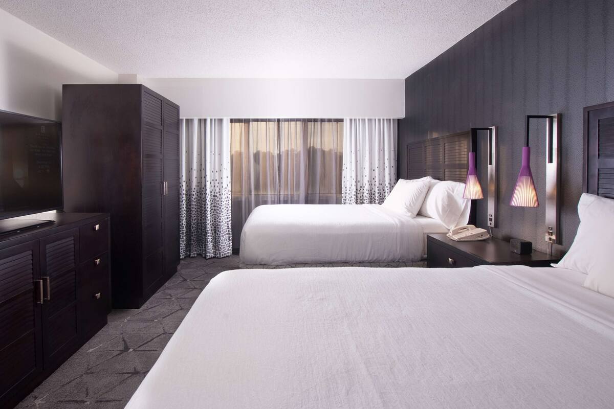 A hotel room with two beds, a TV, a wardrobe, and a large window with curtains.