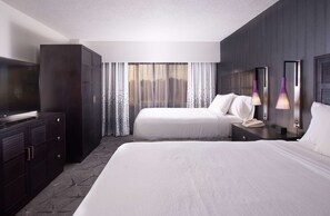 A hotel room with two beds, a TV, a wardrobe, and a large window with curtains.