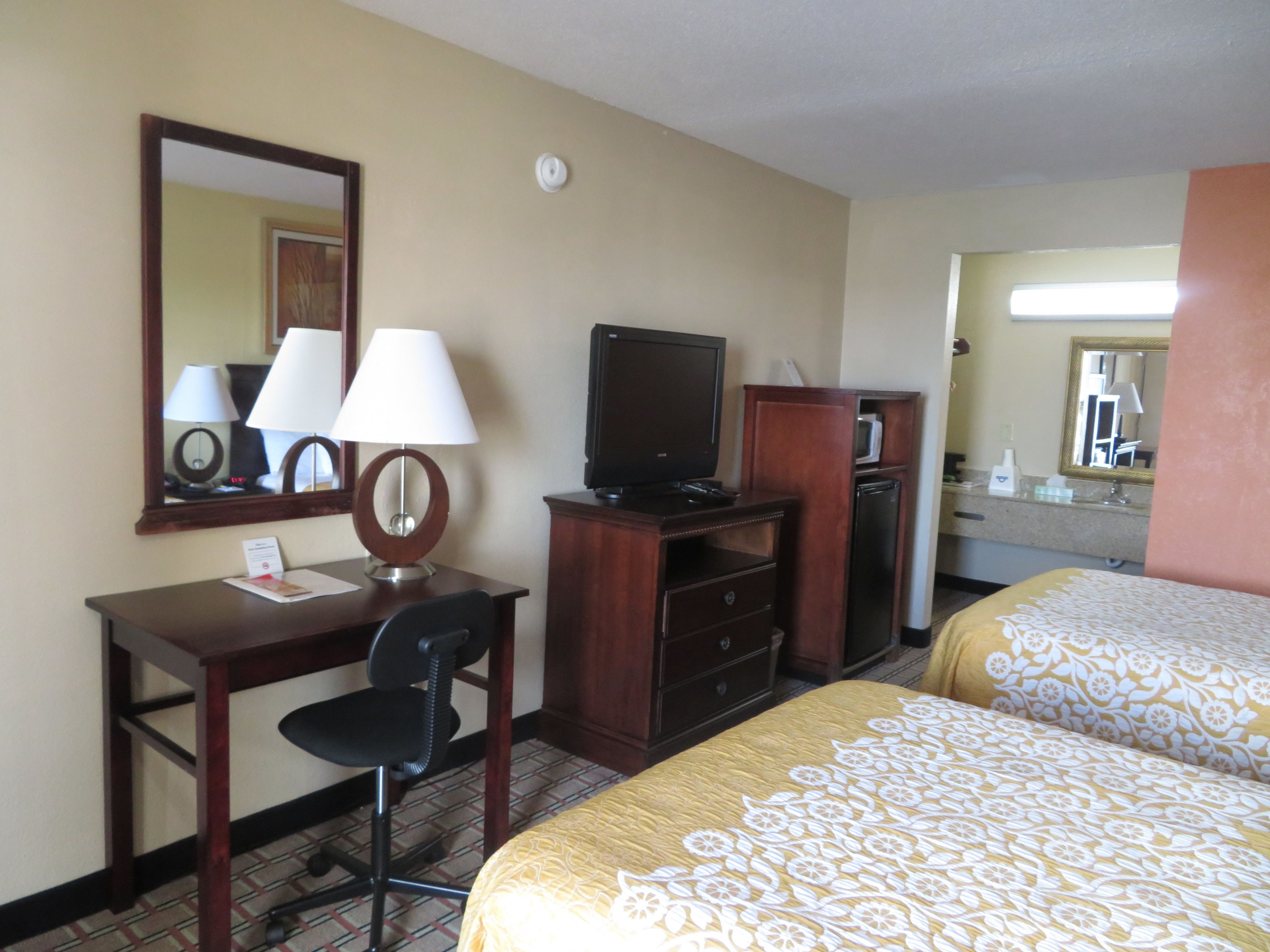 Una habitación de hotel con escritorio, silla, televisor, minibar y dos camas.