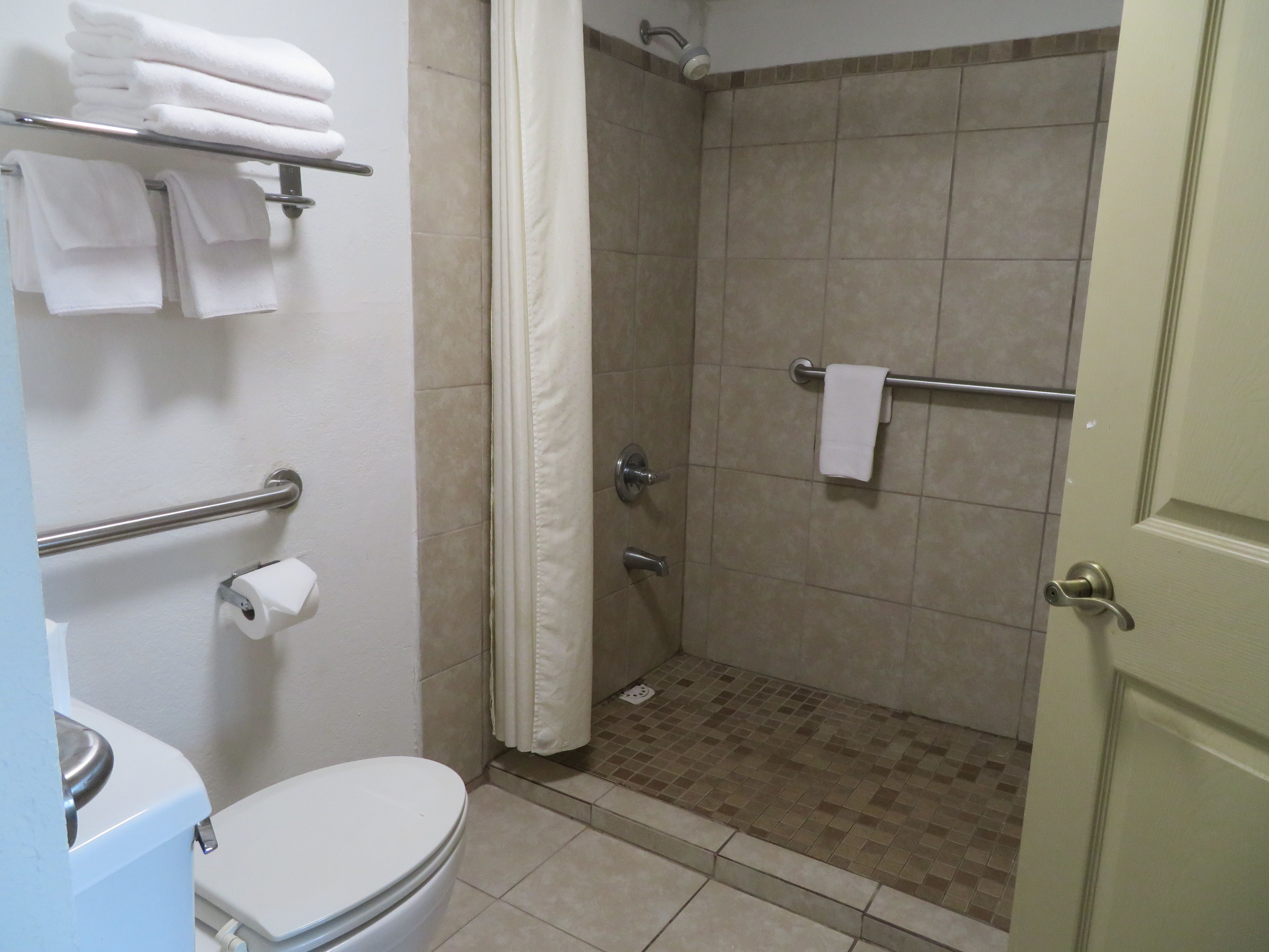 Un baño con inodoro, ducha con puerta de cristal y toallero con toallas dobladas.