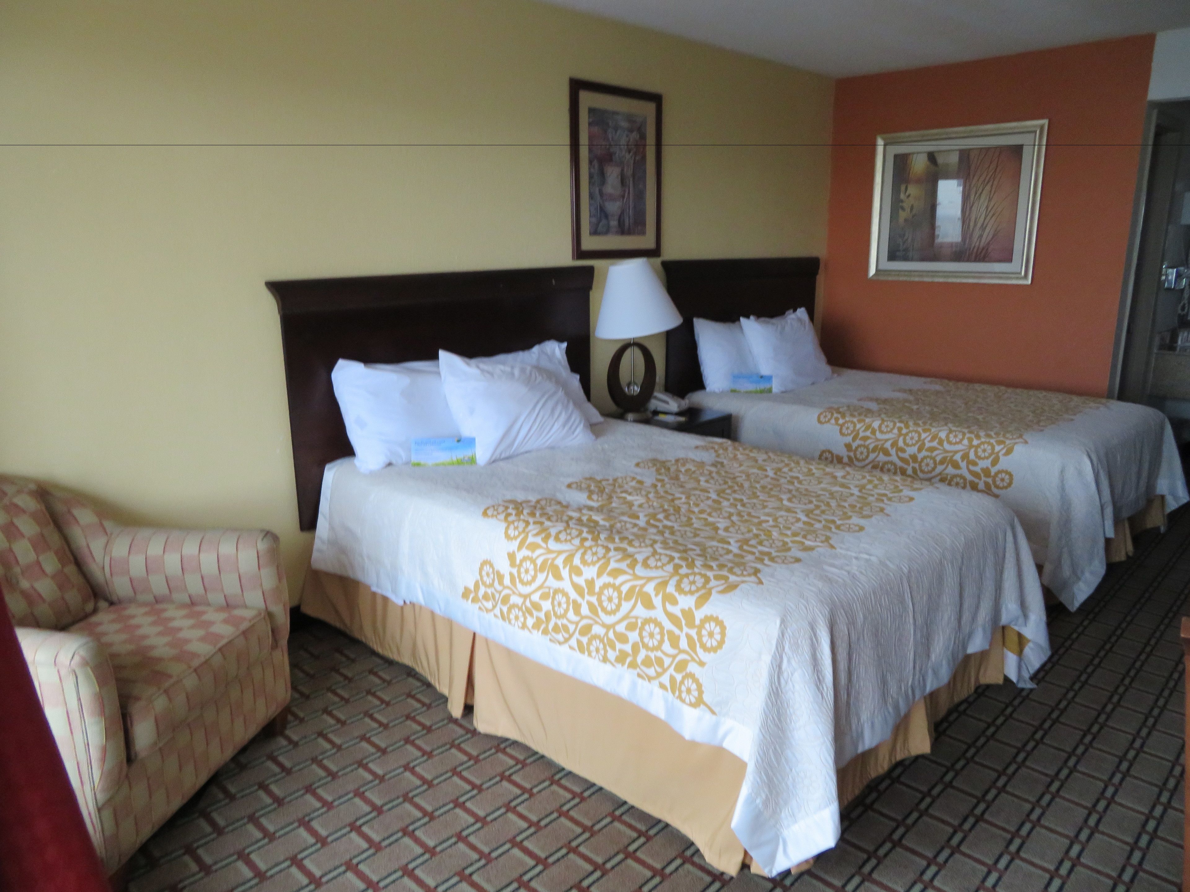 A hotel room with two beds, a chair, a lamp, and a framed picture on the wall.
