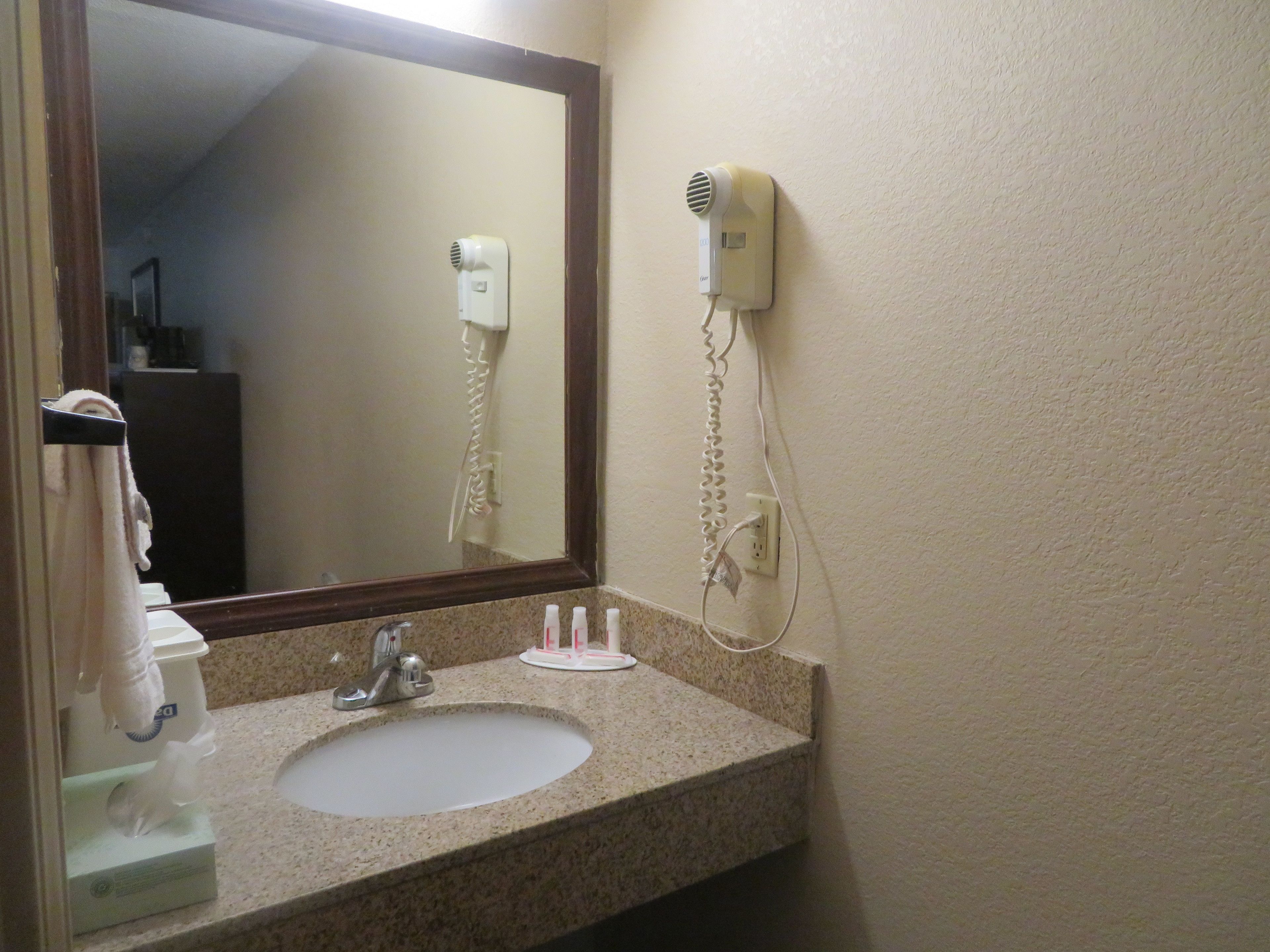 A bathroom with a sink, mirror, and hairdryer mounted on the wall.