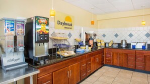 Un área de desayuno con una cafetera, dispensadores de cereales y un cartel que dice 'Daybreak Breakfast'.