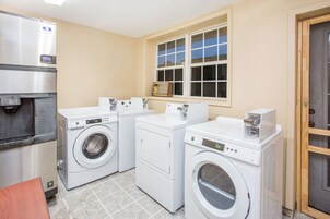 Un cuarto de lavado con dos lavadoras de carga frontal, un secador y un refrigerador de acero inoxidable.