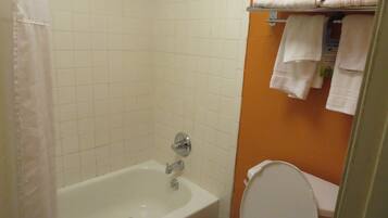 A bathroom with a bathtub, toilet, and a towel rack with folded towels.