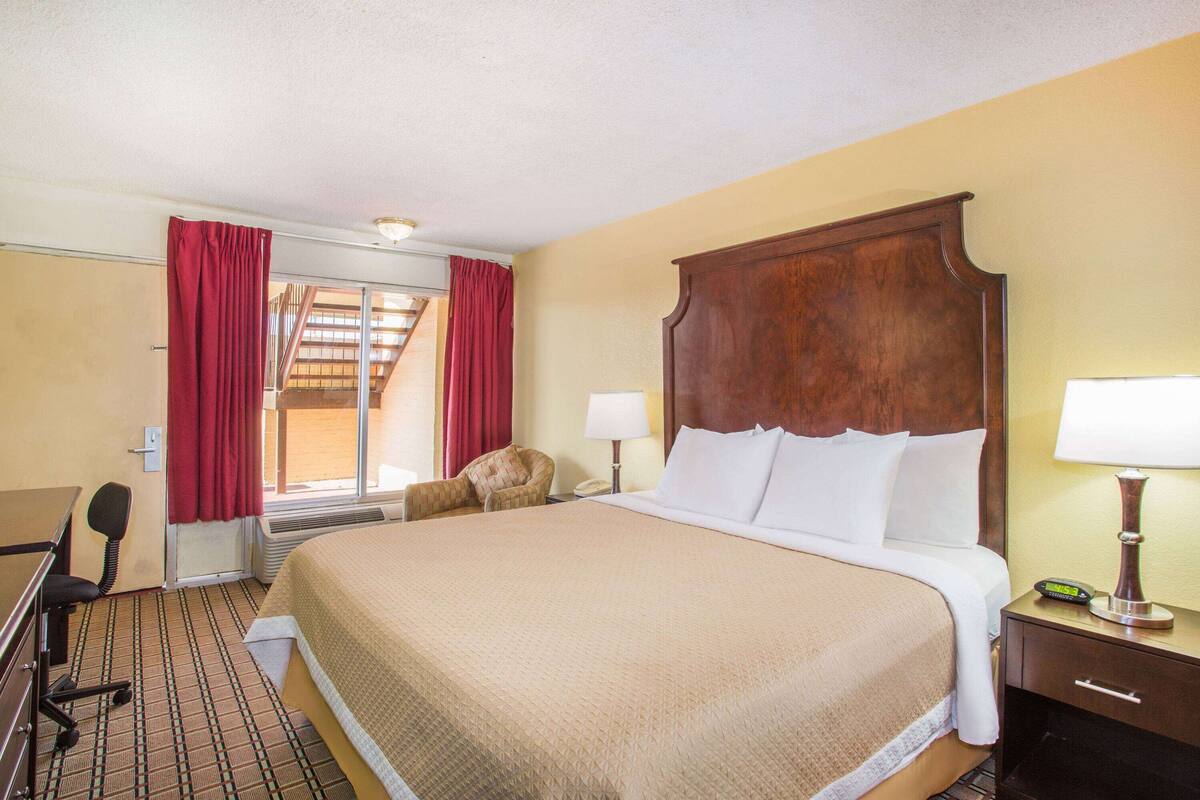 Hotelkamer met een groot bed, een bureau, een stoel, een nachtkastje met een lamp en een raam met gordijnen.
