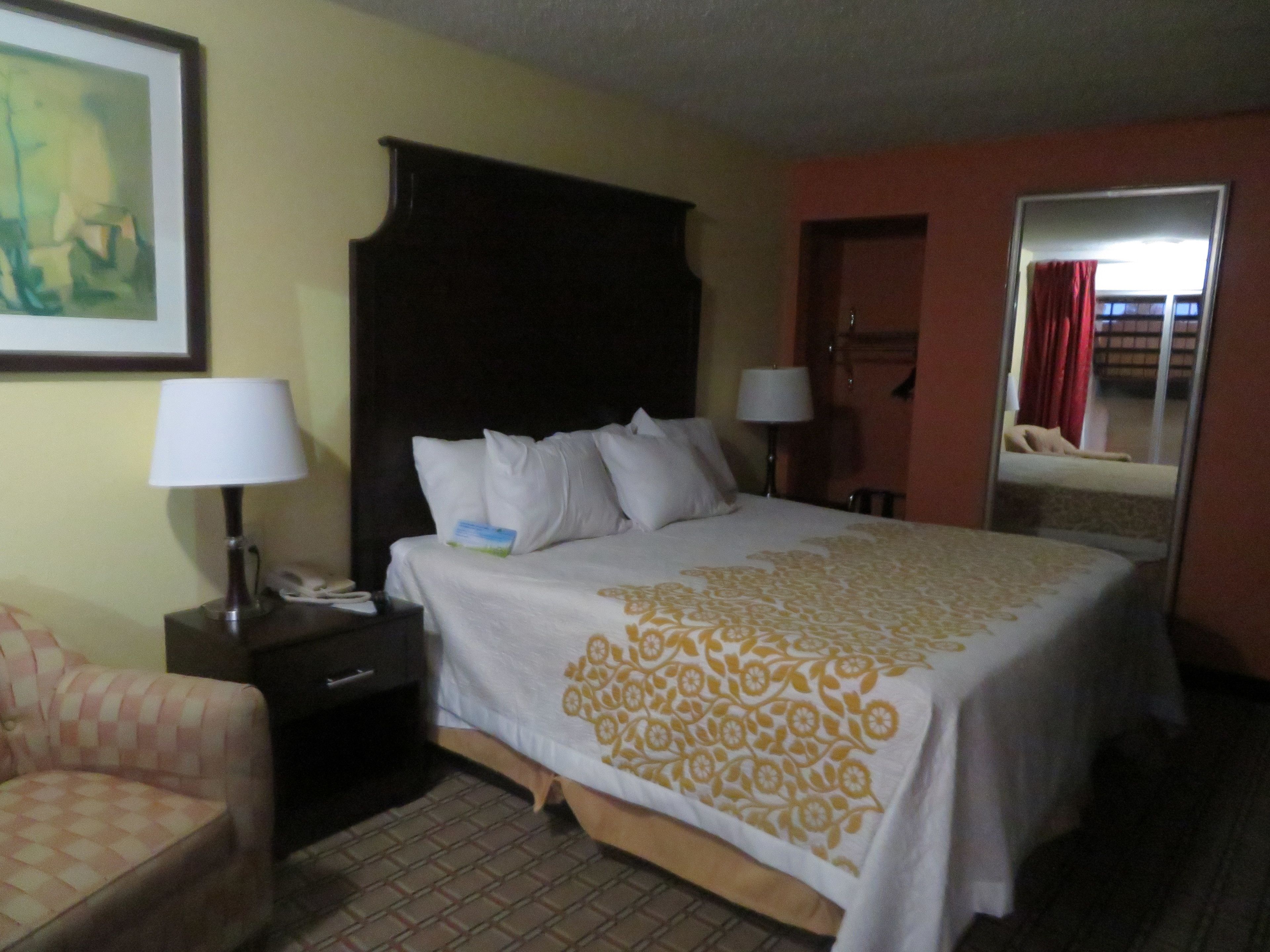 Una habitación de hotel con una cama, dos mesitas de noche, una silla y un espejo.