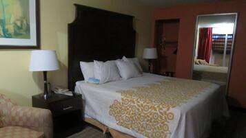 Una habitación de hotel con una cama, dos mesitas de noche, una silla y un espejo.