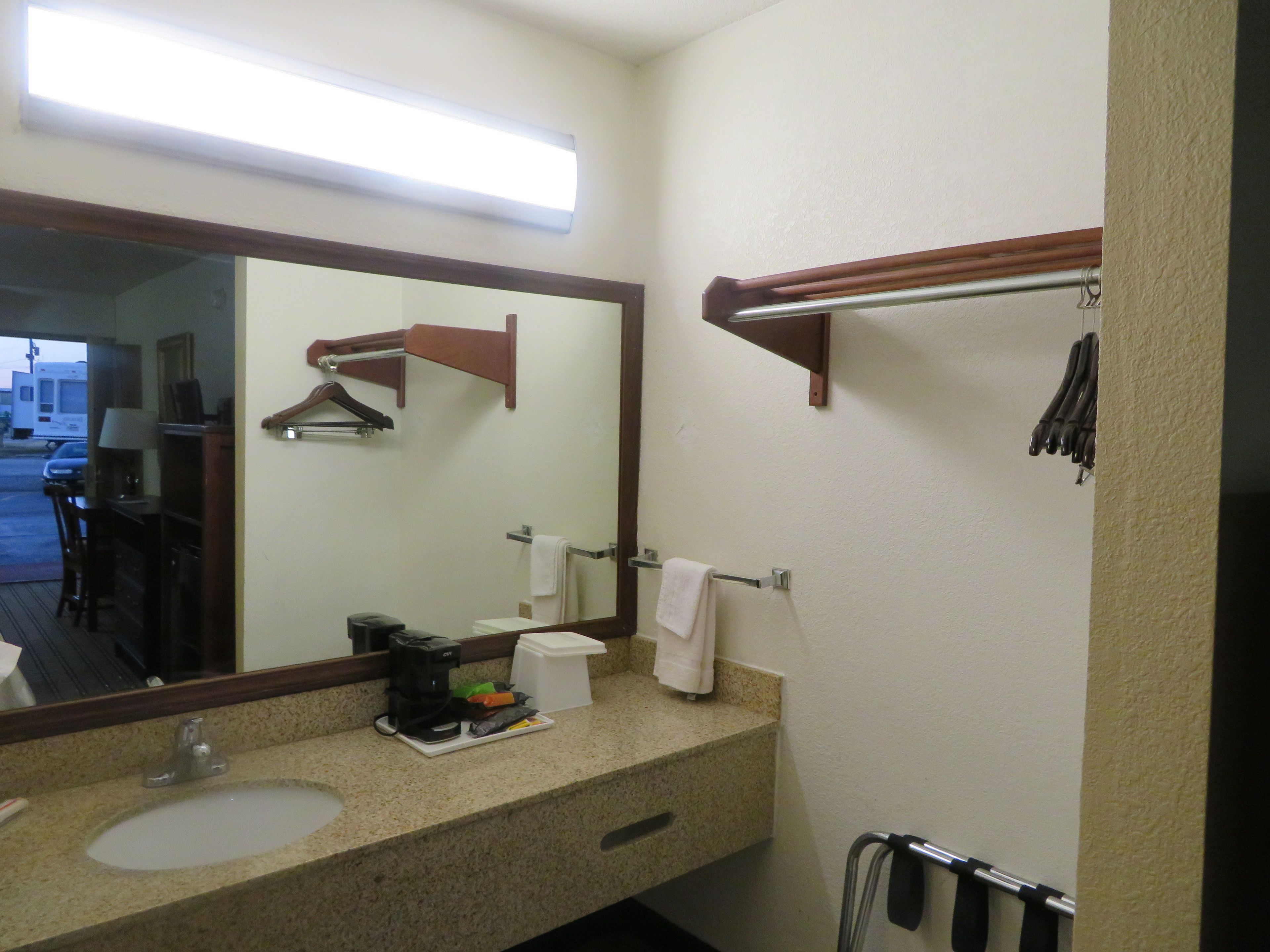 A hotel bathroom with a sink, mirror, towel rack, and a coffee maker on the counter.
