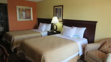 A hotel room with two beds, a nightstand with a lamp, a chair, and two framed pictures on the wall.