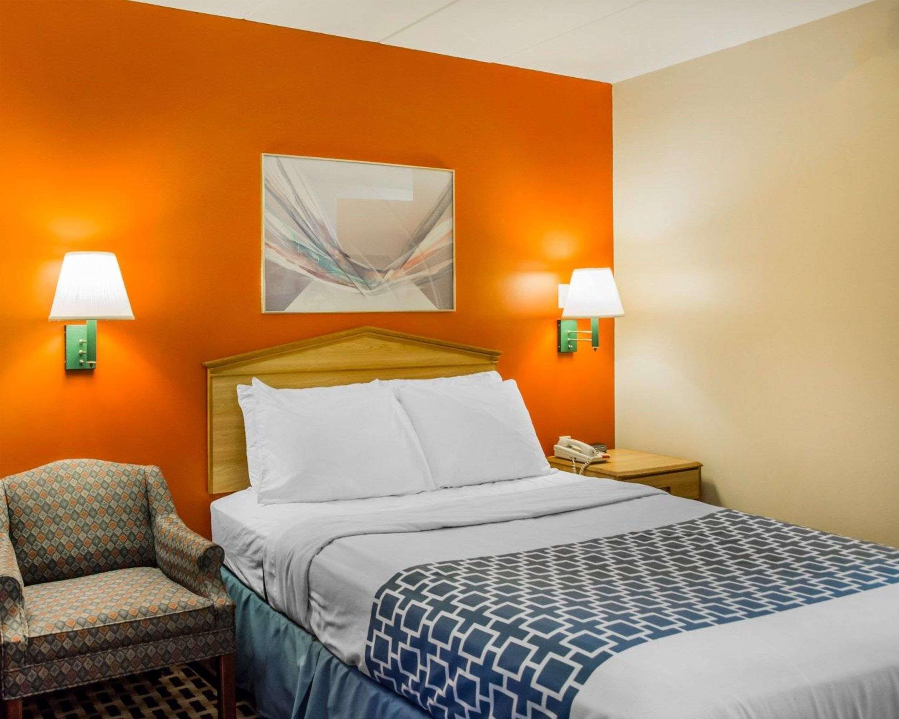 A hotel room with a bed, two chairs, a nightstand with a phone, and wall-mounted lamps.
