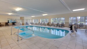 Une piscine intérieure à l’eau d’un bleu cristallin, entourée de chaises longues et d’un espace d’accueil.