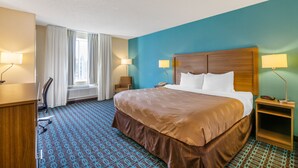 Une chambre d’hôtel avec un grand lit, deux lampes de chevet, un bureau avec une chaise et une fenêtre avec des rideaux.