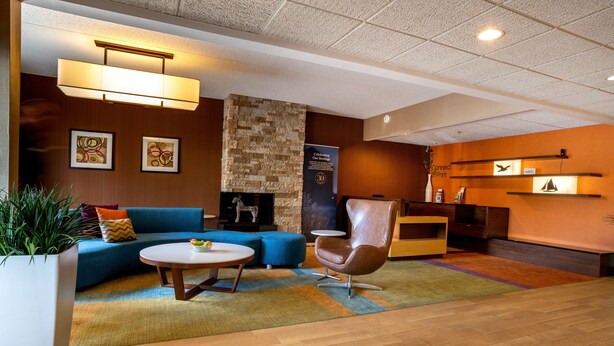 Un hall d’hôtel moderne avec un canapé bleu, une table basse ronde, un fauteuil en cuir et une cheminée en pierre.
