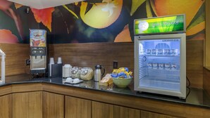 Un bar pour prendre le petit-déjeuner, équipé d’une machine à café et d’un réfrigérateur rempli de boissons, ainsi qu’une fresque colorée sur le mur.