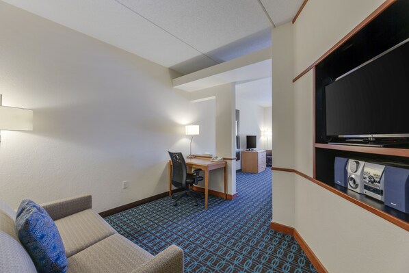 Une chambre d’hôtel équipée d’un canapé, d’un bureau, d’une chaise, d’une télévision et dont le sol est recouvert d’une moquette.