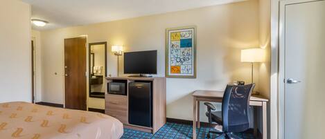 A hotel room with a bed, a desk with a chair, a television, a refrigerator, and a microwave.