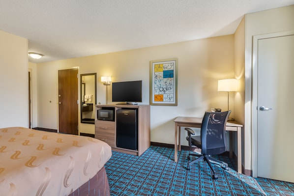 A hotel room with a bed, a desk with a chair, a television, a refrigerator, and a microwave.