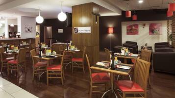 A restaurant interior with wooden tables and chairs, a bar area, and a seating section with sofas.