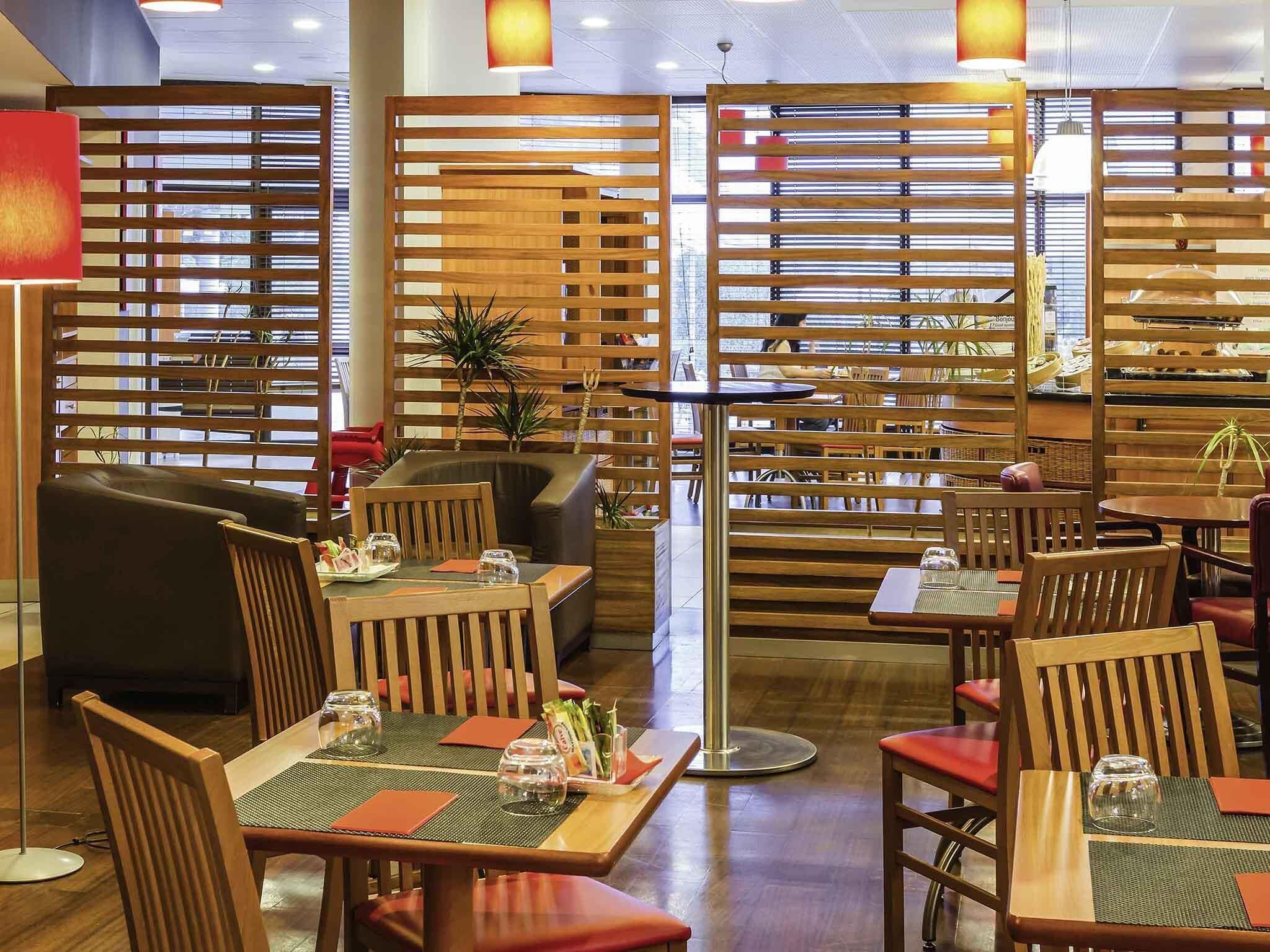 A restaurant with wooden partitions, tables with red cushions, and a modern interior design.
