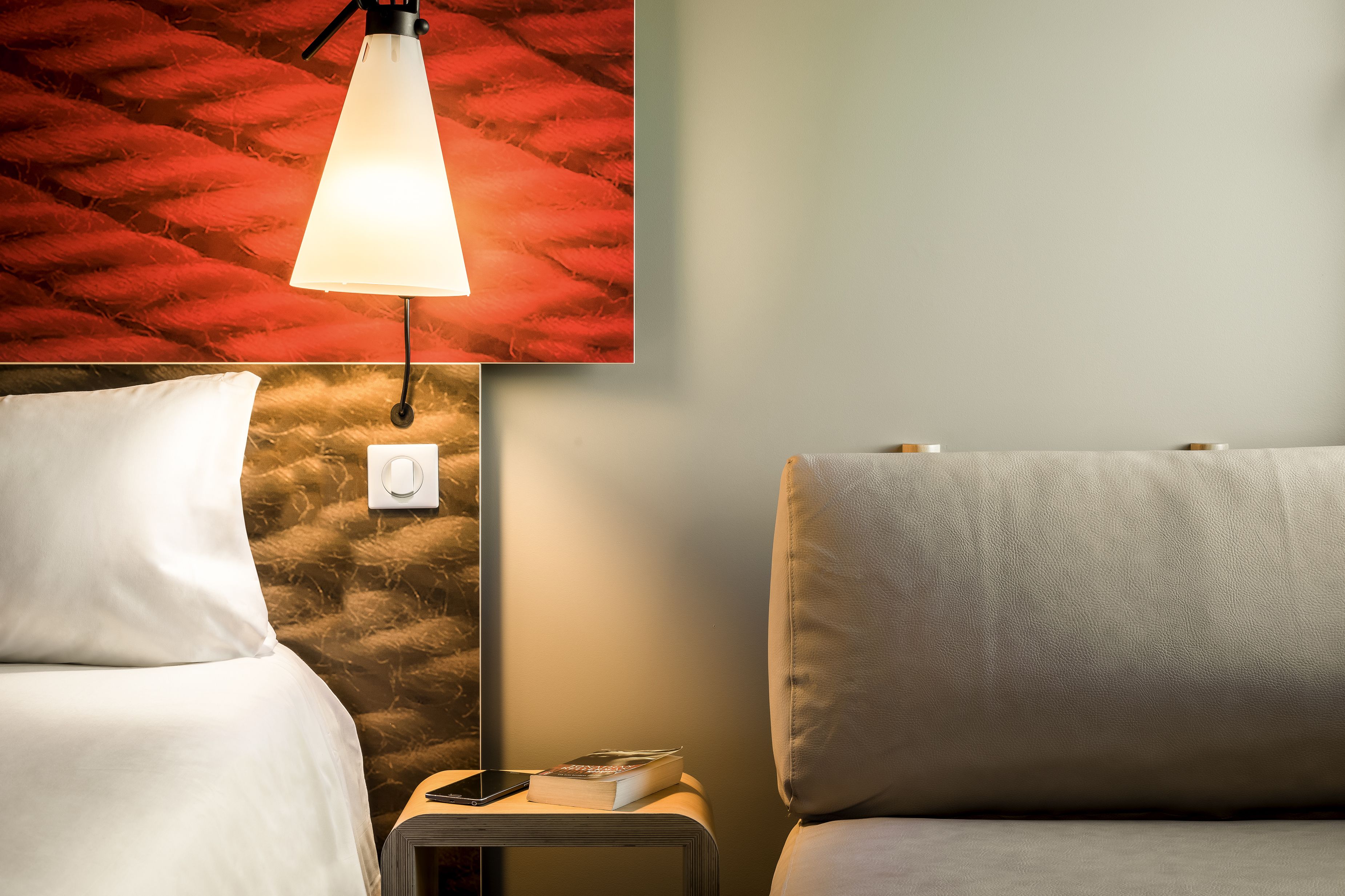 Une chambre d’hôtel avec un lit, une table de chevet, une lampe et un mur orné d’un motif texturé.