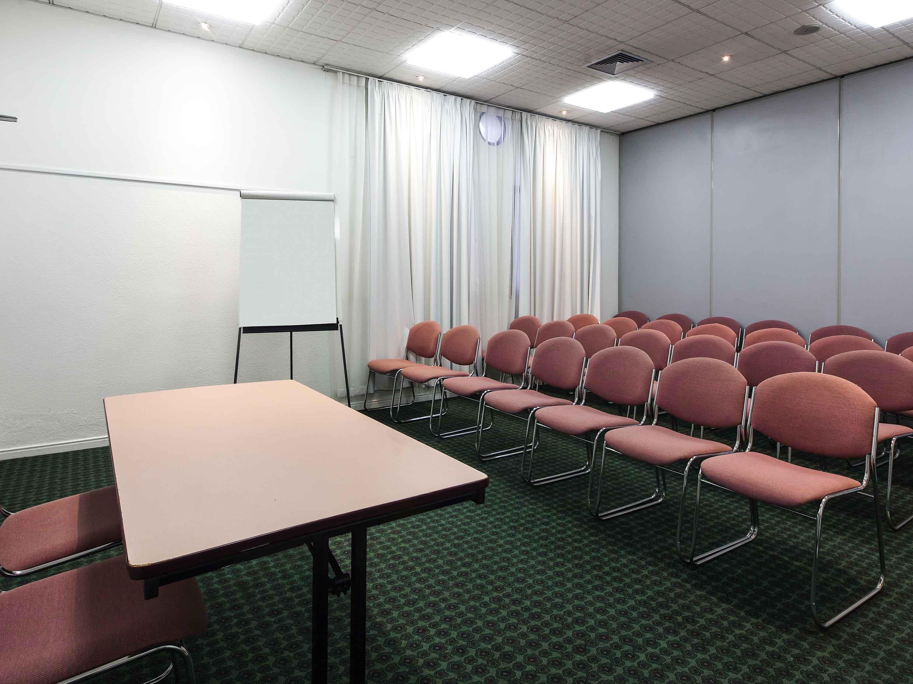 Una sala de conferencias con una mesa, sillas, una pizarra y una cortina.