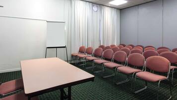 Una sala de conferencias con una mesa, sillas, una pizarra y una cortina.
