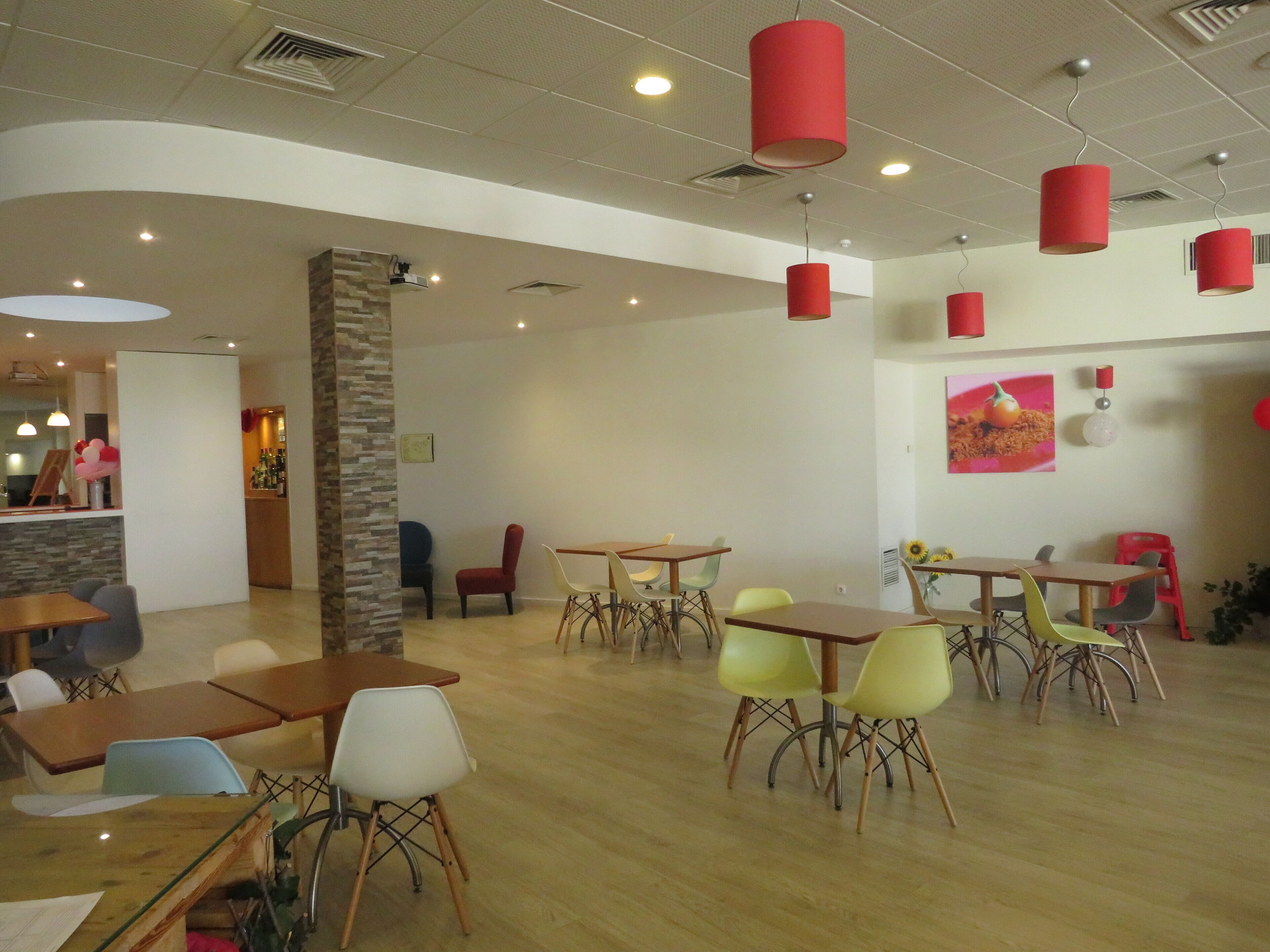 Un vaste espace intérieur doté de nombreuses tables et chaises, d’un pilier en pierre et de lampes rouges suspendues.