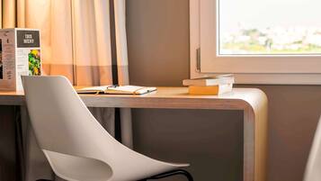 A modern hotel room with a desk, a white chair, and a window with a view of a cityscape.