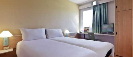 A hotel room with two beds, a desk with a computer, a lamp, and a TV on a stand.