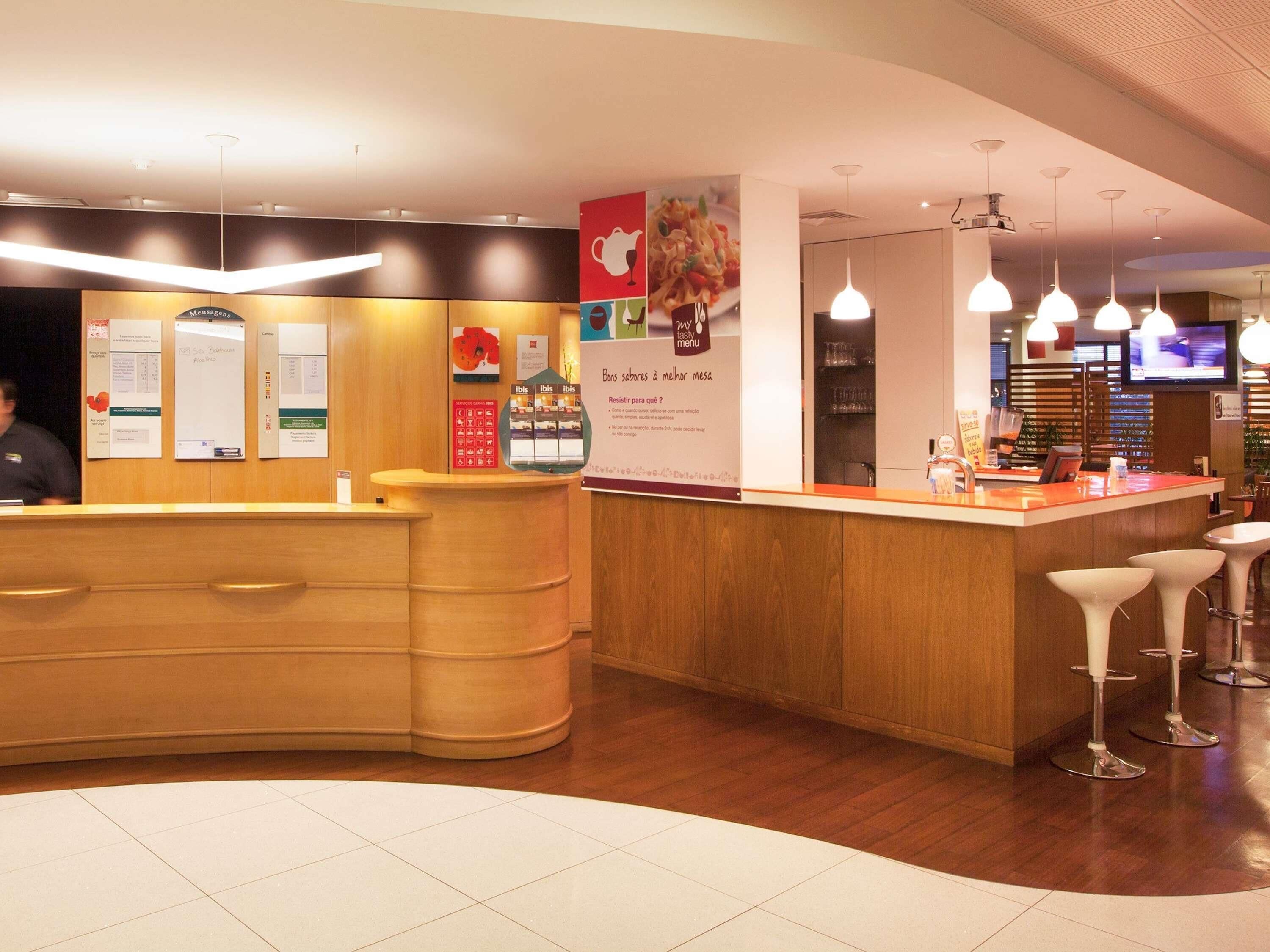 A reception area with a wooden counter, a digital menu board, and a seating area with bar stools.
