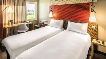 A hotel room with two beds, a desk, a chair, a window with a view, and a red textured wall.