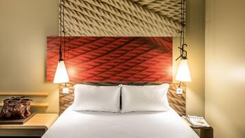 Una habitación de hotel con una cama, dos lámparas de noche, una mesita de noche con un bolso y una revista sobre la mesita.