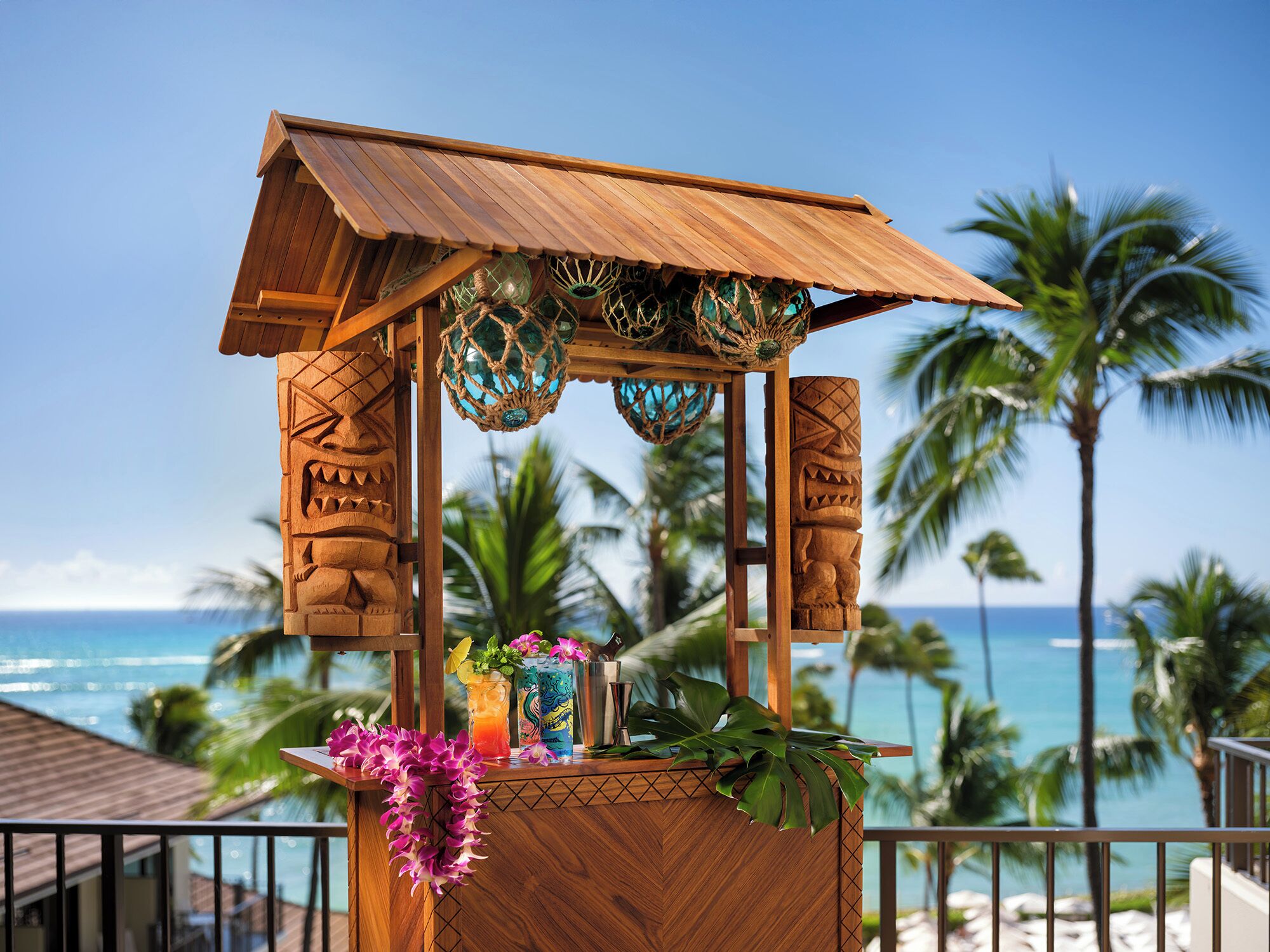 A wooden tiki bar with a view of the ocean and palm trees.