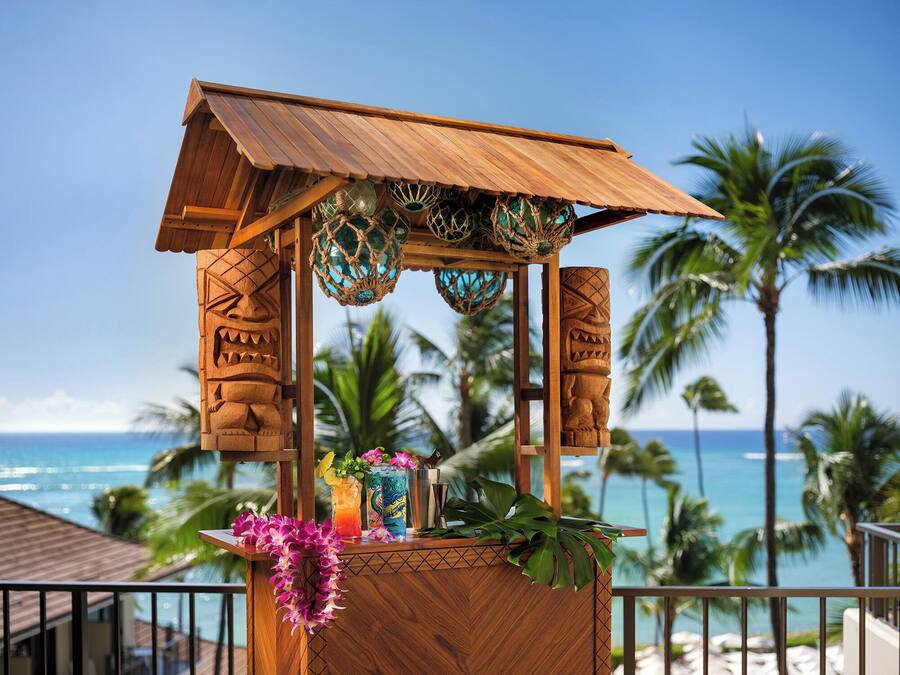 A wooden tiki bar with a view of the ocean and palm trees.