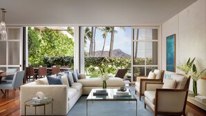 A modern living room with a large window, a sofa, a coffee table, and a dining area. - Halekulani (Honolulu)