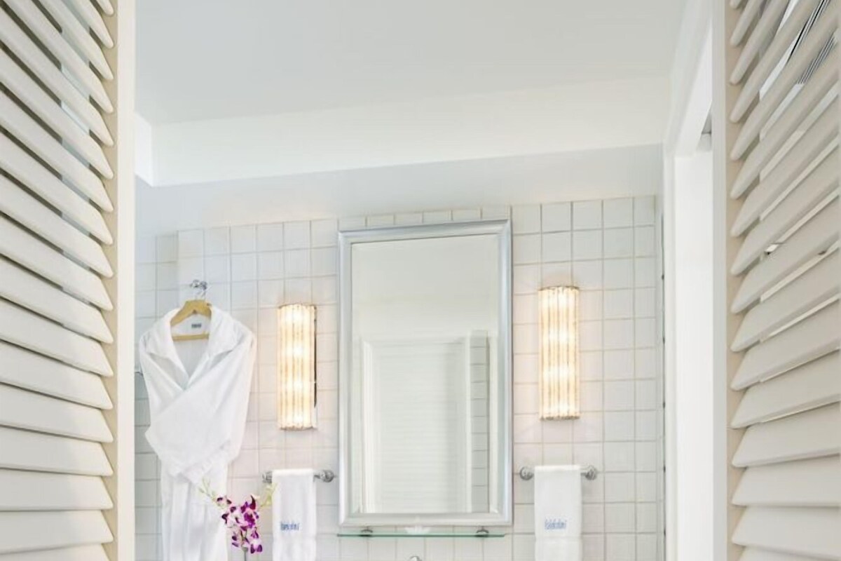 A bathroom with a white tiled wall, a wooden vanity, a mirror, a towel rack, and a small wooden stool.