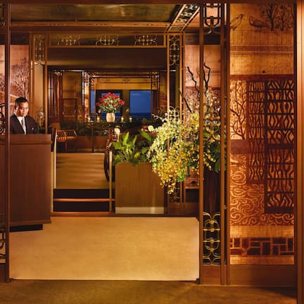 A reception area with a wooden reception desk, a large vase with flowers, and a decorative screen with intricate patterns.