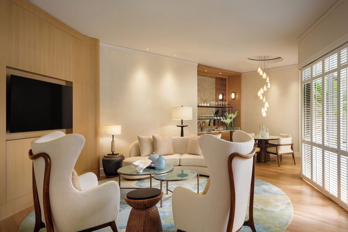 A modern living room with a sofa, two armchairs, a coffee table, and a TV mounted on the wall.