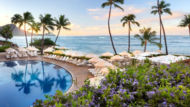 A poolside area with lounge chairs and umbrellas, overlooking a beach and ocean. - Halekulani (Honolulu)